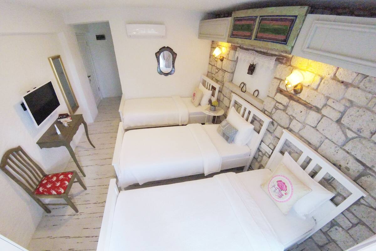 A room with three single beds, a TV, a chair, and a stone wall.