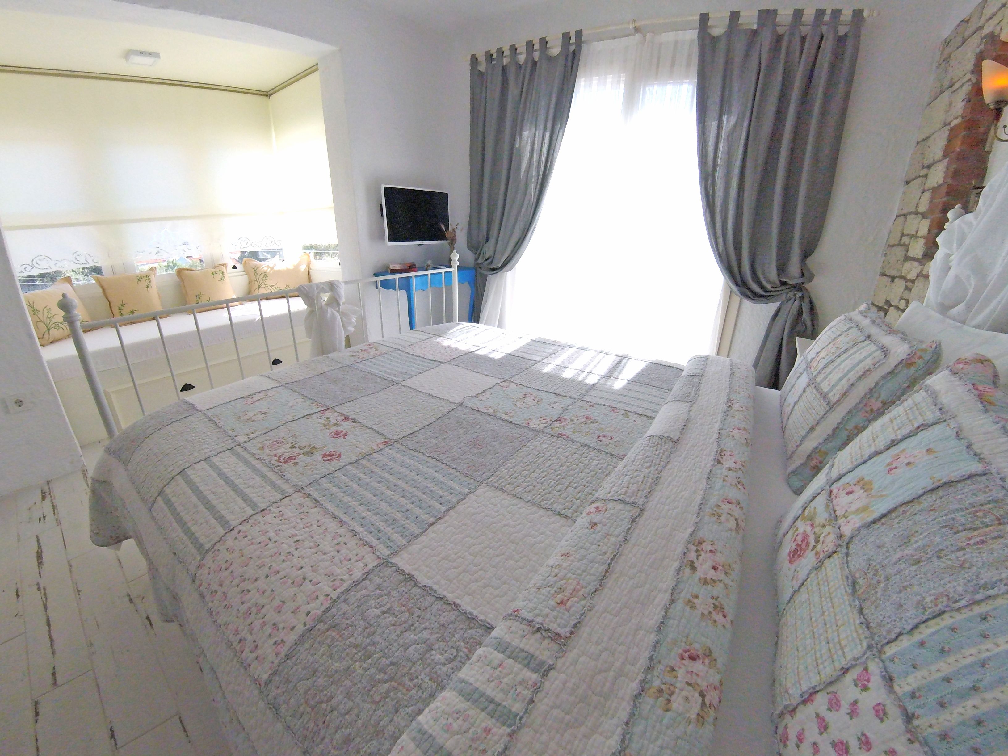 A bedroom with a bed, a TV, and a window with curtains.