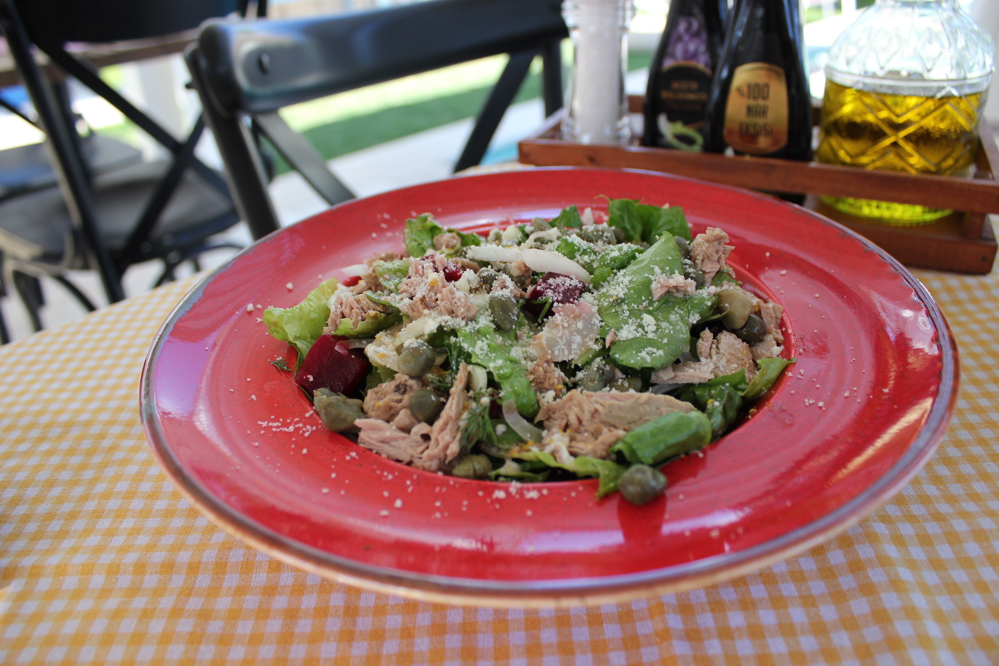 A red plate with a salad on a yellow and white checkered tablecloth.