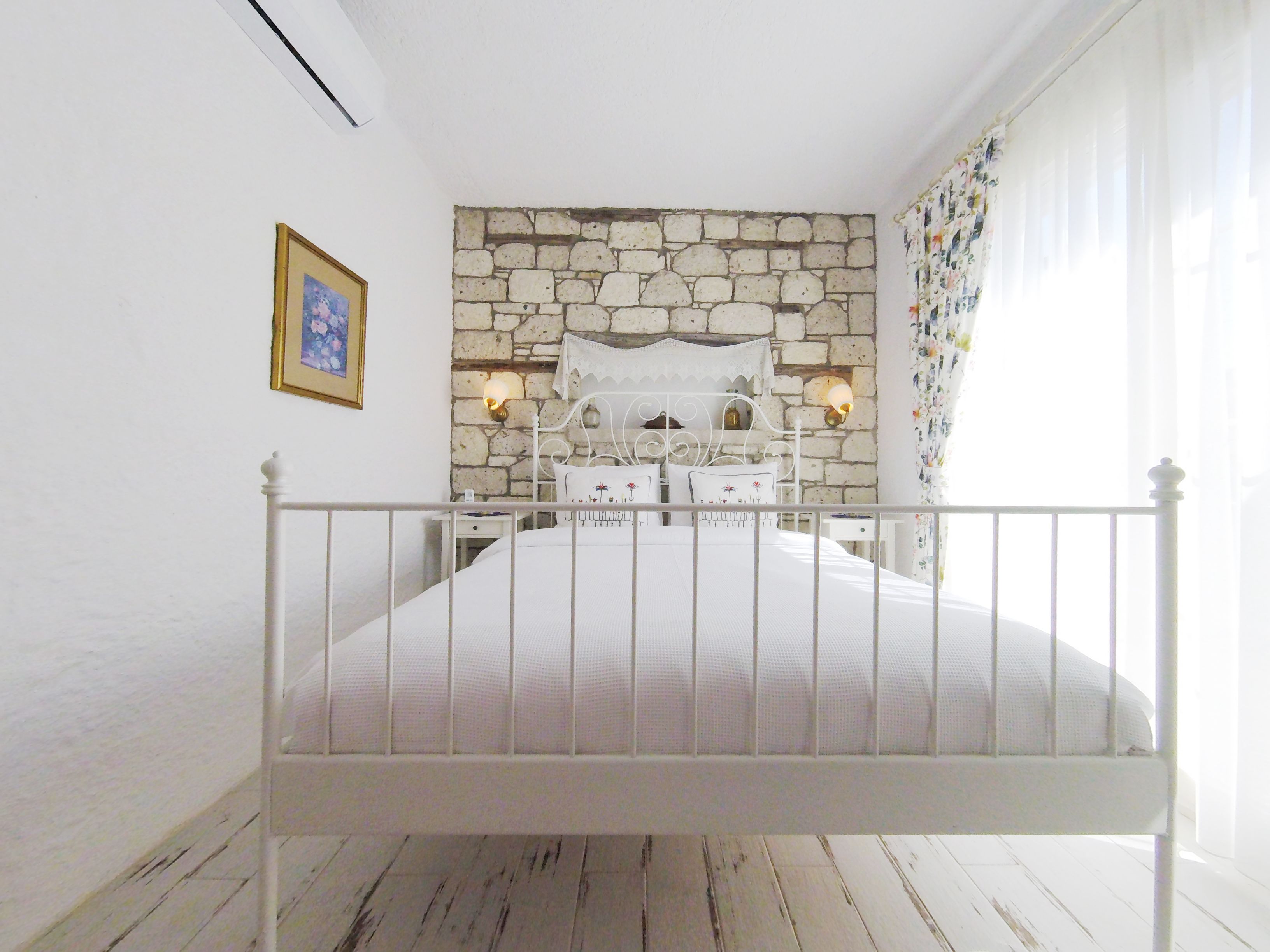 A bedroom with a stone wall, a bed with a white headboard, two bedside tables, and a nightstand.