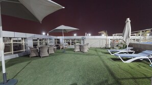 Une terrasse extérieure avec un revêtement de gazon synthétique, des meubles en osier et des parasols.