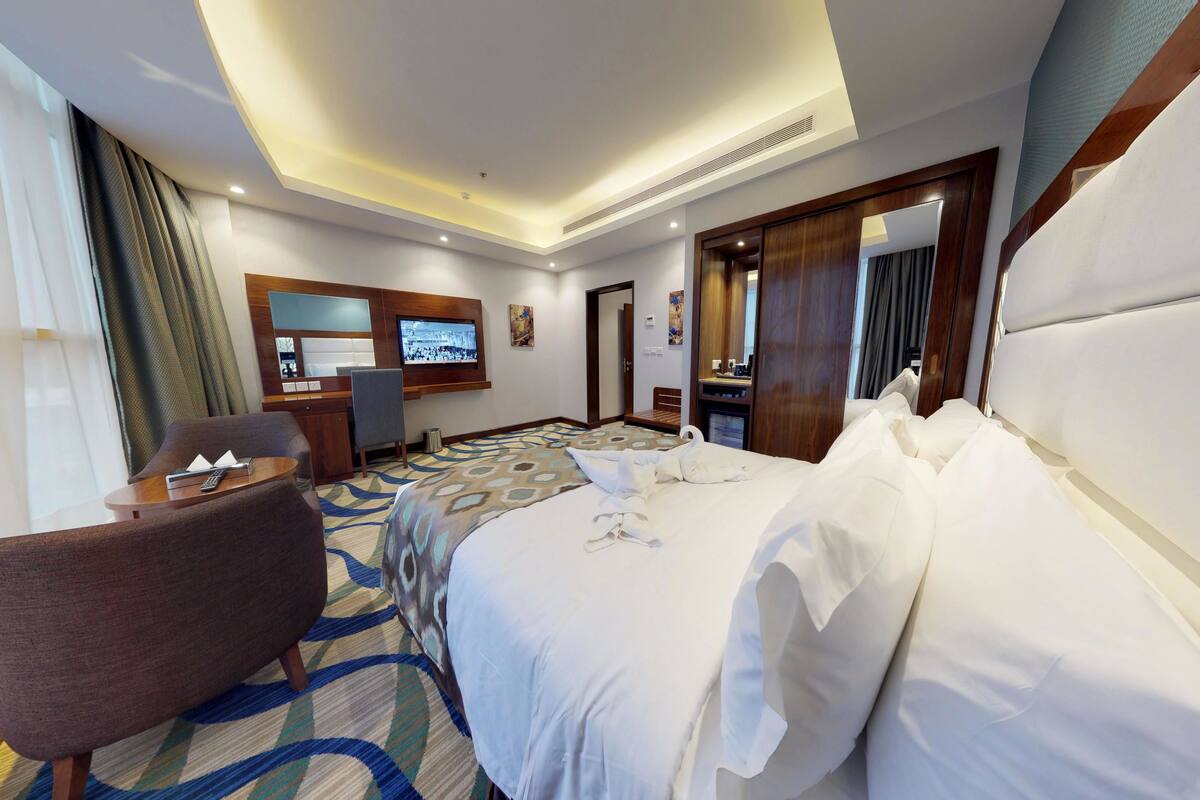 A hotel room with a large bed, a desk, a chair, and a television.