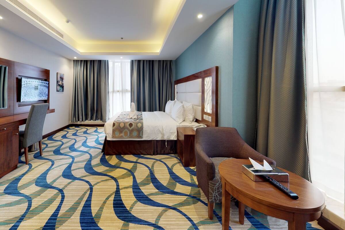A hotel room with a bed, a desk, a chair, a TV, and a patterned carpet.