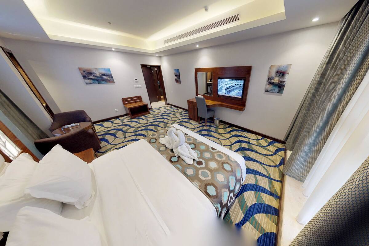 A hotel room with a bed, a desk, a chair, a TV, and artwork on the walls.
