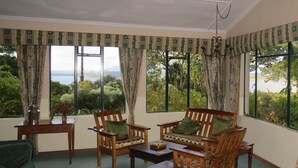 Habitación con vistas a un jardín y montañas, amoblada con sillas y una mesa de madera.