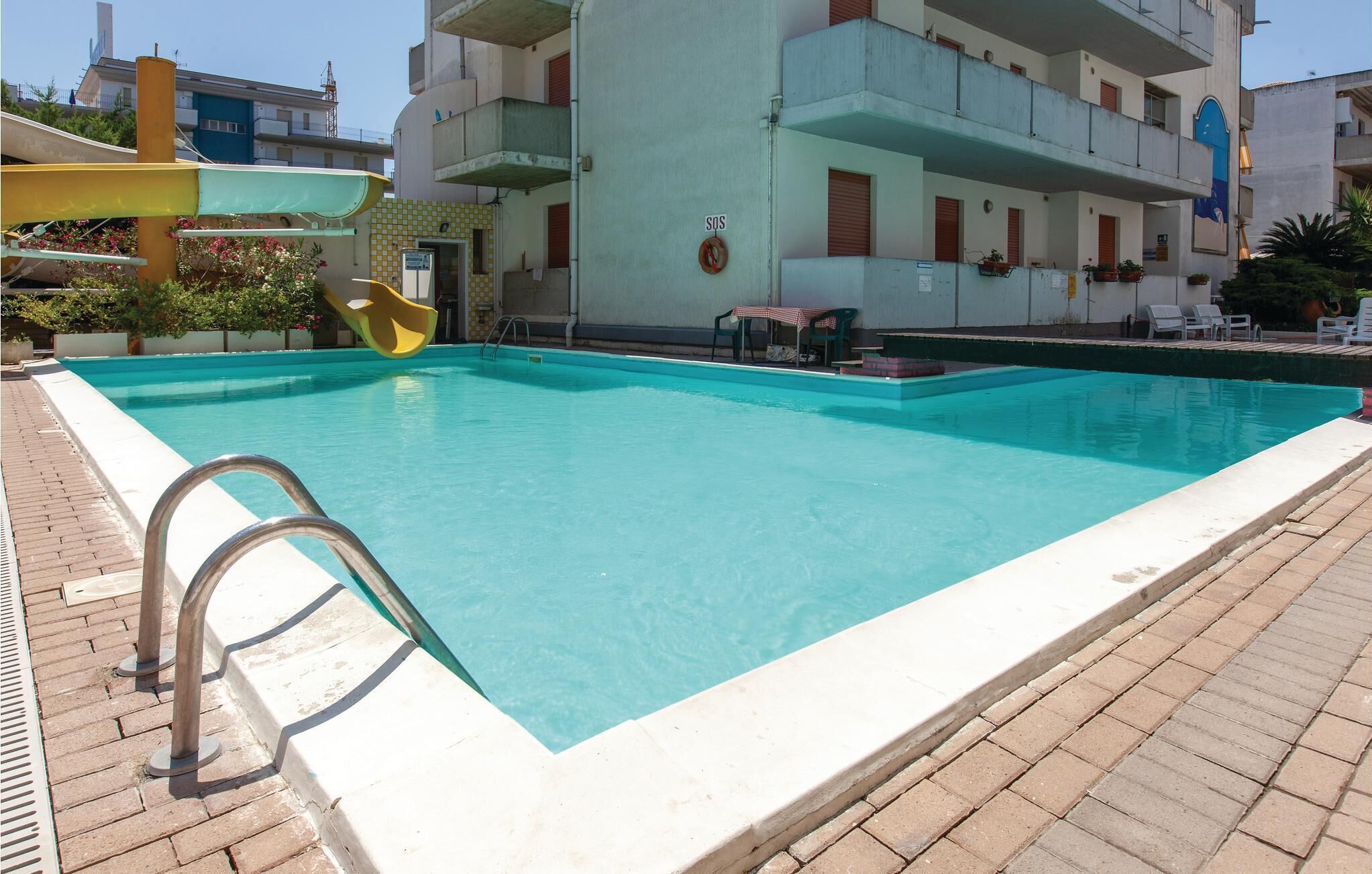 Una piscina rectangular con una escalera metálica en el lado izquierdo, rodeada por un solárium con baldosas.
