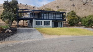 A modern two-story house with a balcony, surrounded by a well-maintained lawn and a gravel driveway.