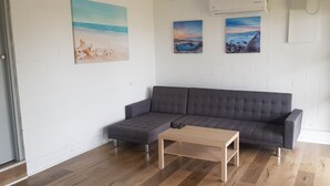 A modern living room with a grey sofa, a wooden coffee table, and three beach-themed paintings on the wall.