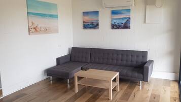 A modern living room with a grey sofa, a wooden coffee table, and three beach-themed paintings on the wall.