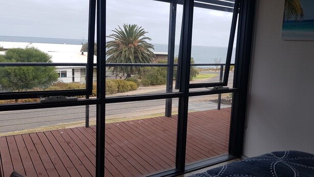 A room with a large window overlooking a wooden deck and a road.