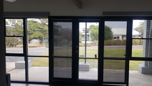 A view through a sliding glass door with a metal grill, leading to a paved area with a grassy lawn and a building in the background.