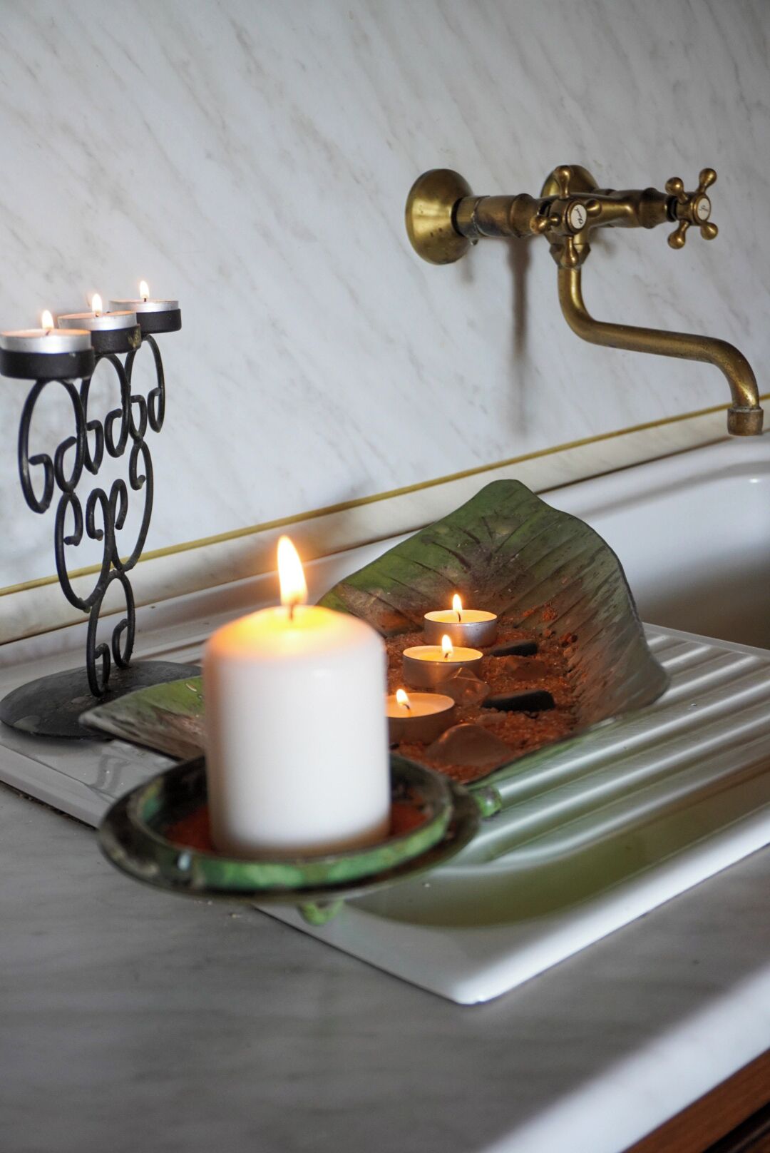 Un lavamanos con grifo de latón, una vela blanca y un candelabro decorativo de metal con velas.