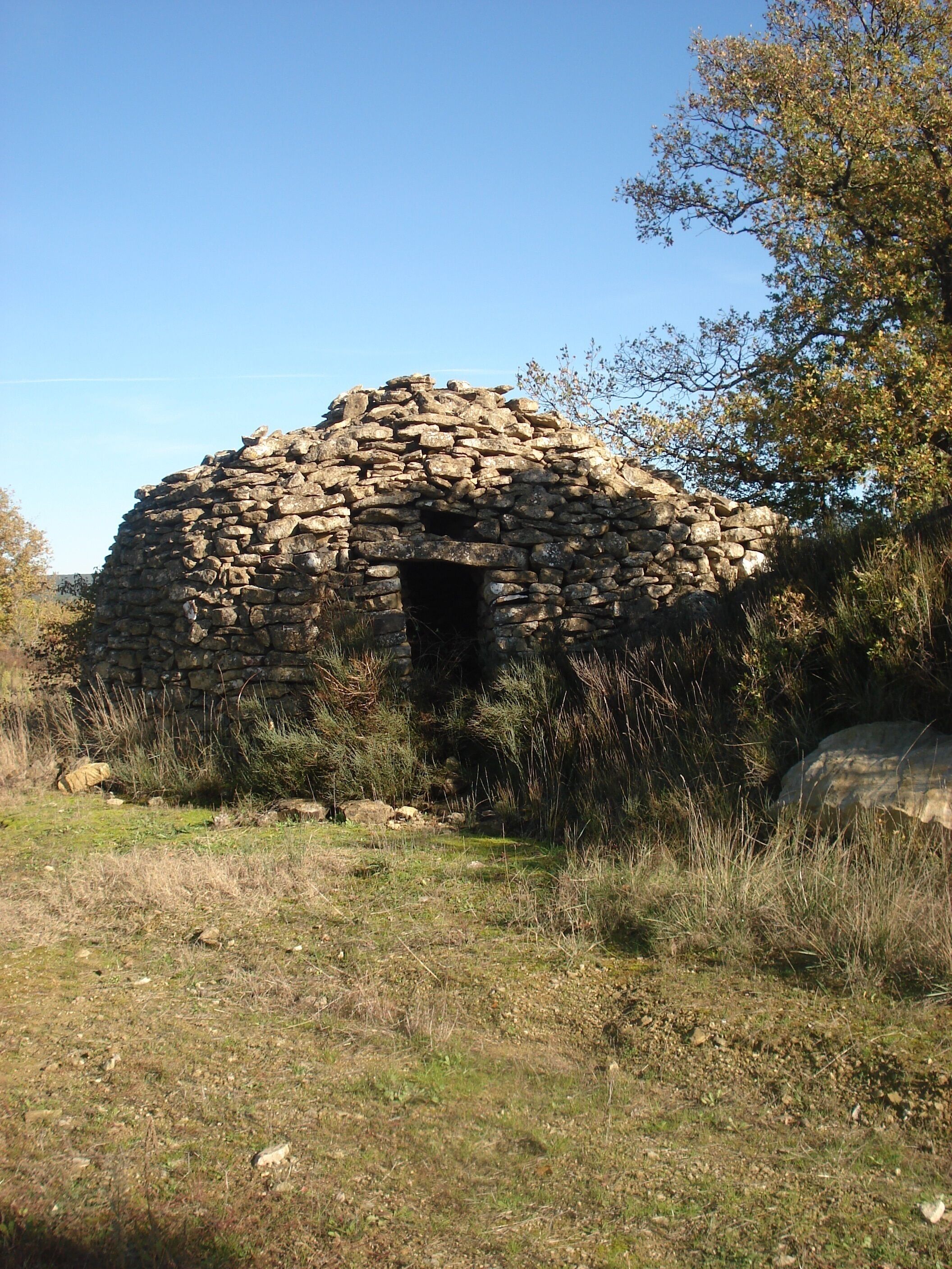 A stone structure with a central opening, surrounded by grass and shrubs.