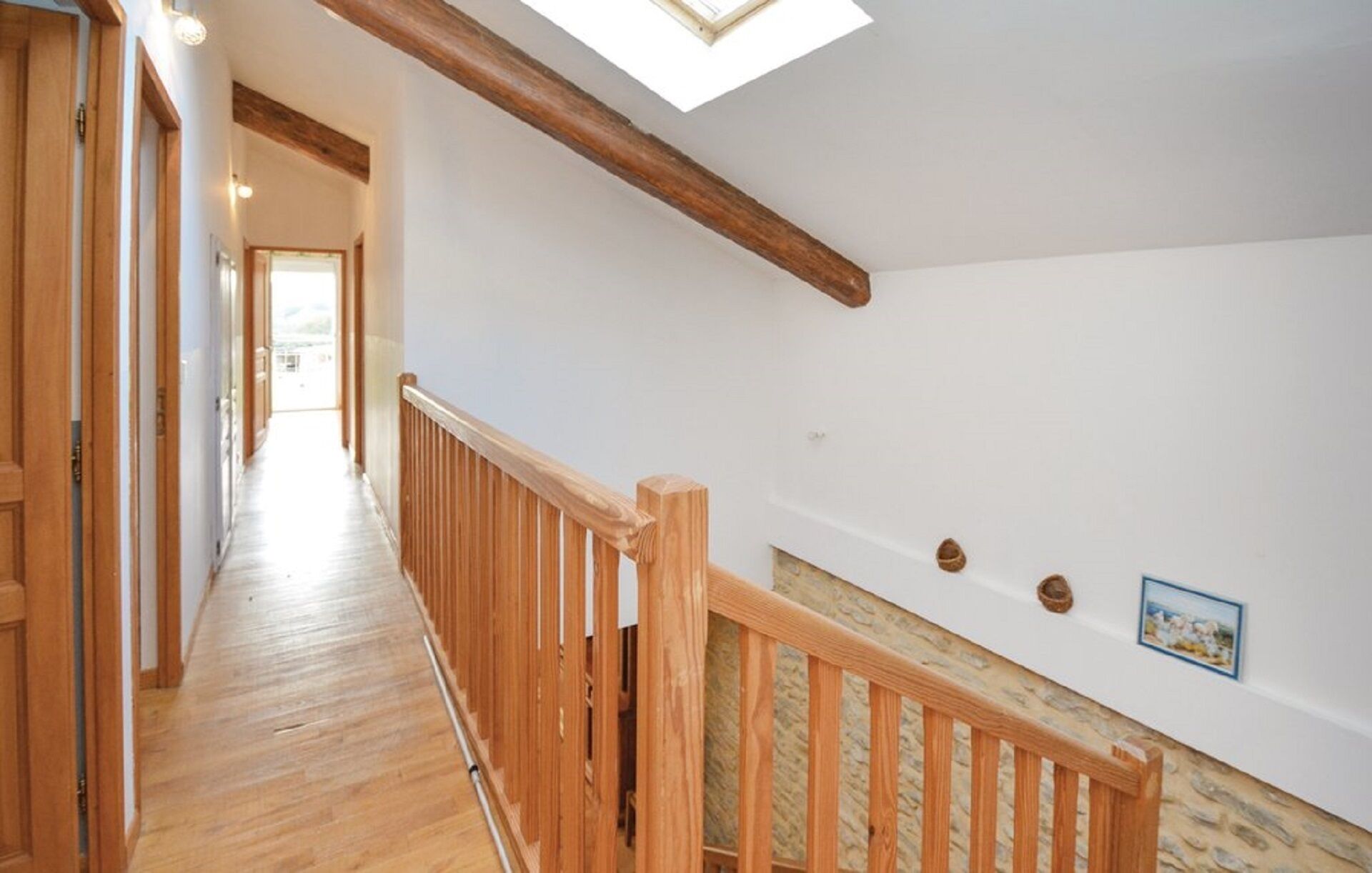 Un escalier en bois, surmonté d’une lucarne, mène à une pièce aux murs blancs et à un mur d’accent en pierre.