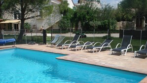 Une piscine à l’eau d’un bleu cristallin, entourée de chaises longues et d’une terrasse en pierre.