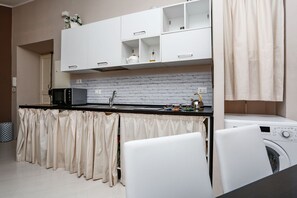 Cocina compacta con microondas, lavamanos y lavadora, con armarios blancos y salpicadero de azulejos.