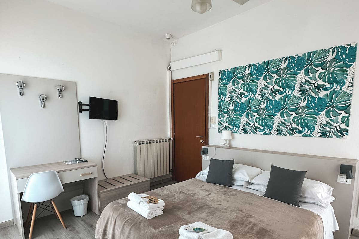 A modern bedroom with a bed, a desk, a chair, a ceiling fan, and a wall-mounted TV.