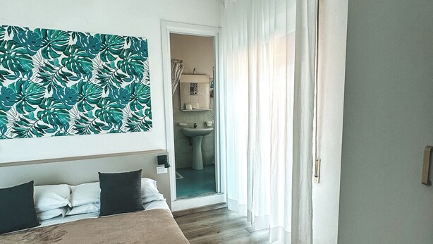 A hotel room with a bed, a bathroom visible through an open door, and a large abstract wall art piece. - Hotel Maremola (Pietra Ligure)