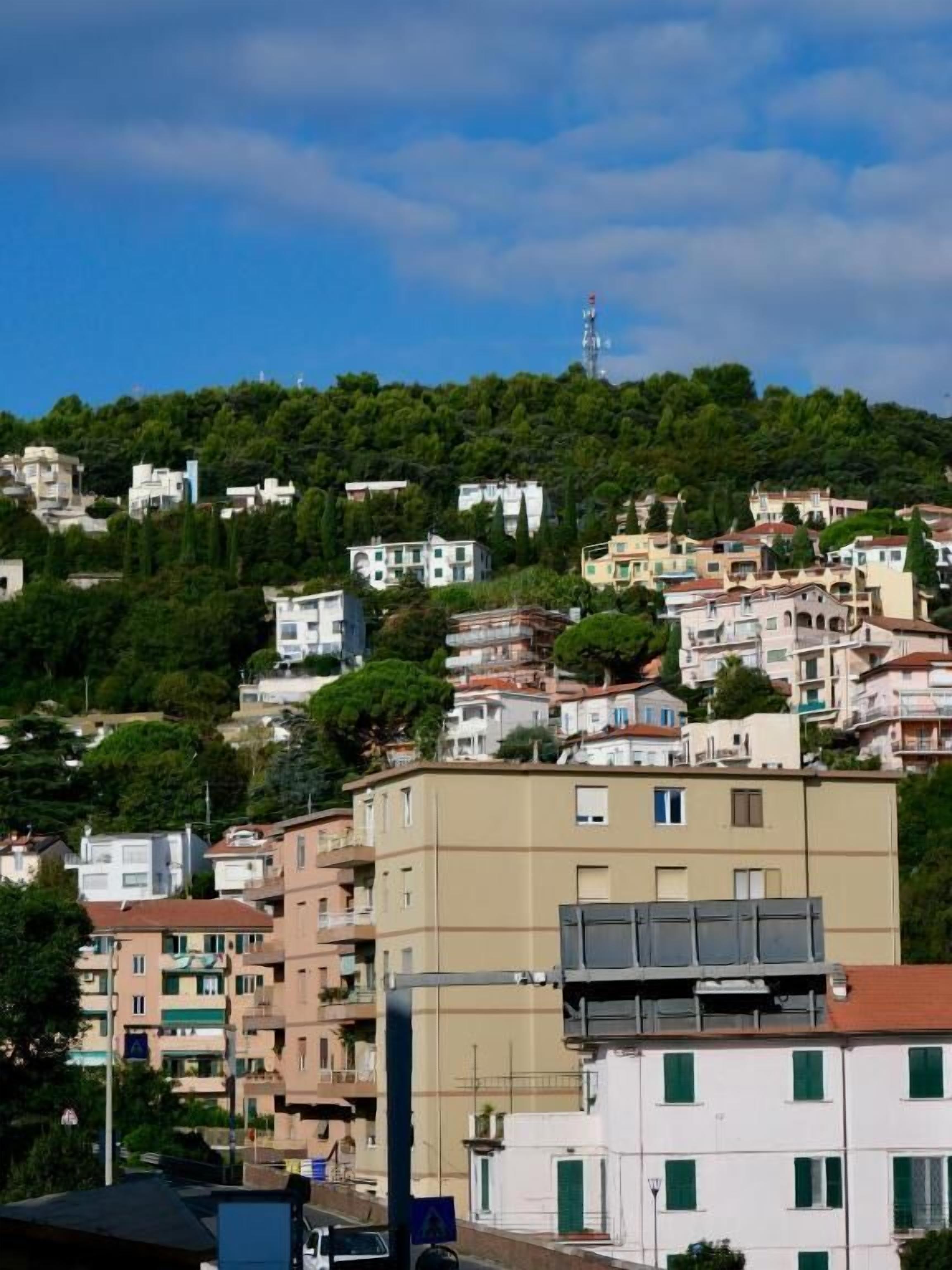 Un quartier résidentiel composé d’immeubles à plusieurs étages, dont certains sont dotés de balcons, et une colline couverte d’une végétation luxuriante en arrière-plan.