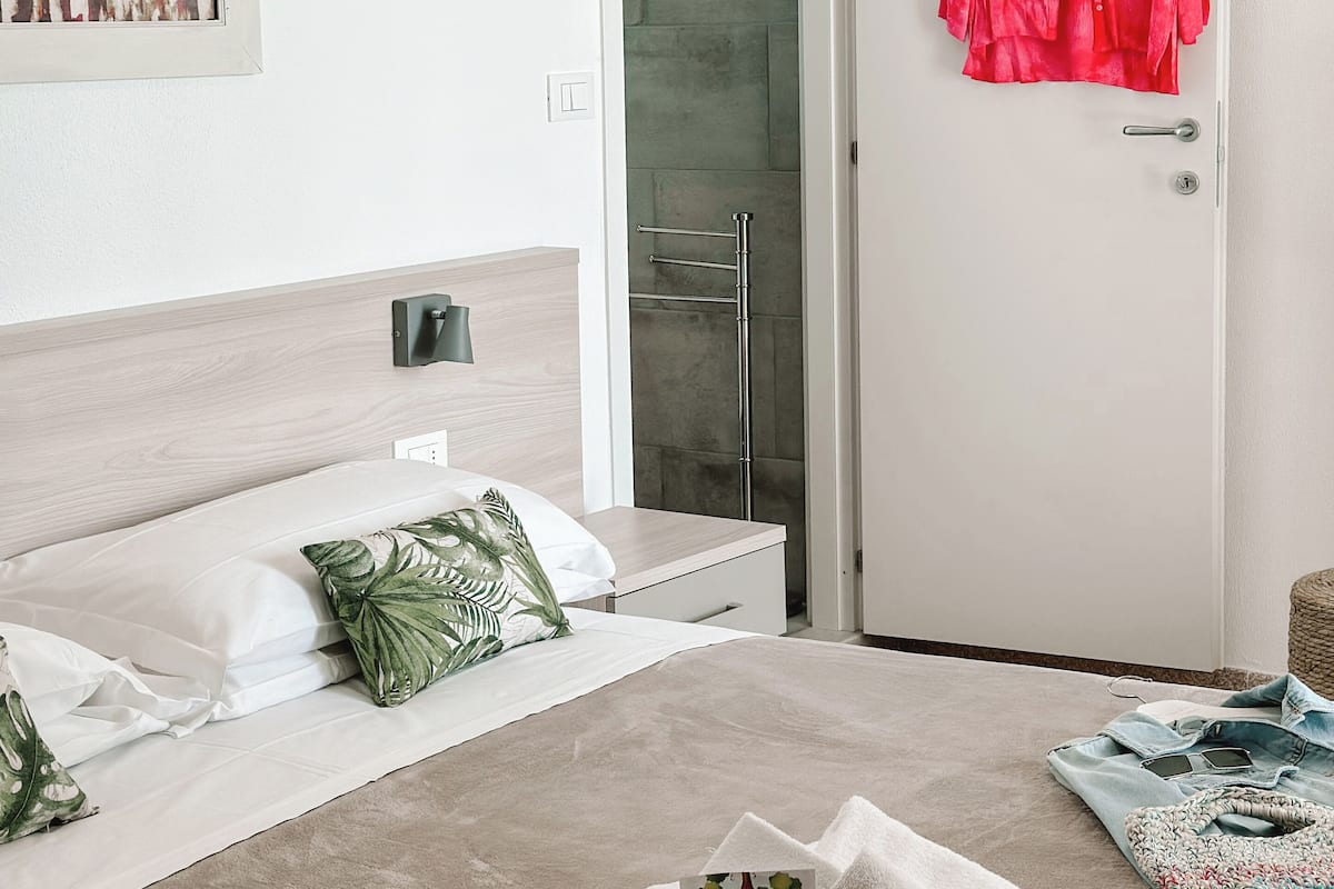A hotel room with a bed, a shower area, and a door with a red garment hanging on it.