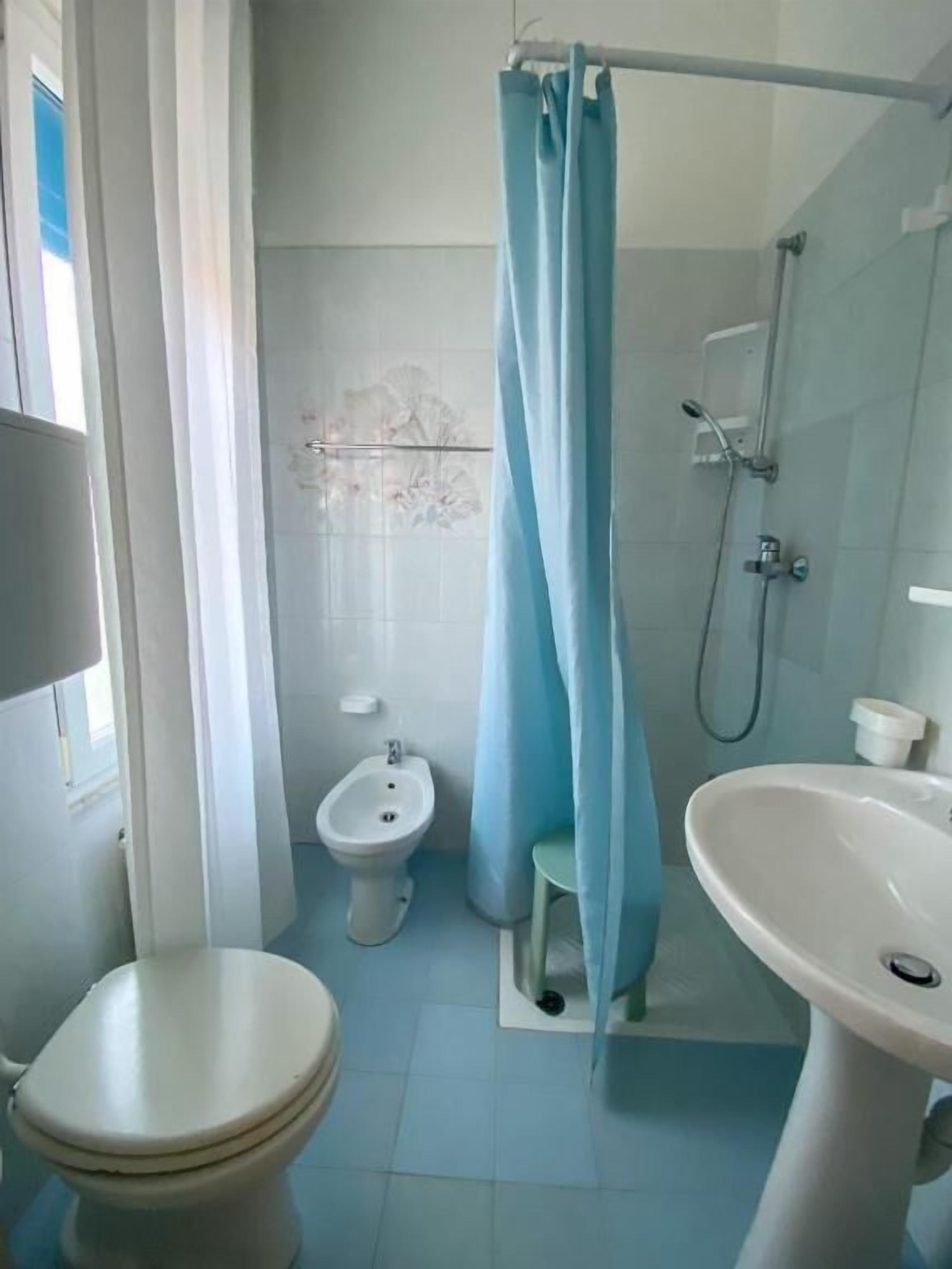 A bathroom with a toilet, bidet, shower, and sink.