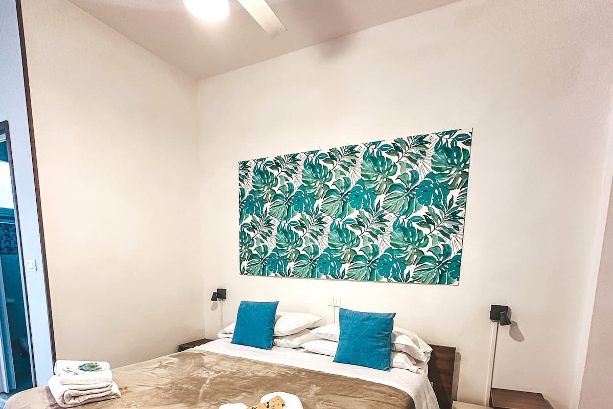 A hotel room with a bed, a ceiling fan, a wall art, and a nightstand.