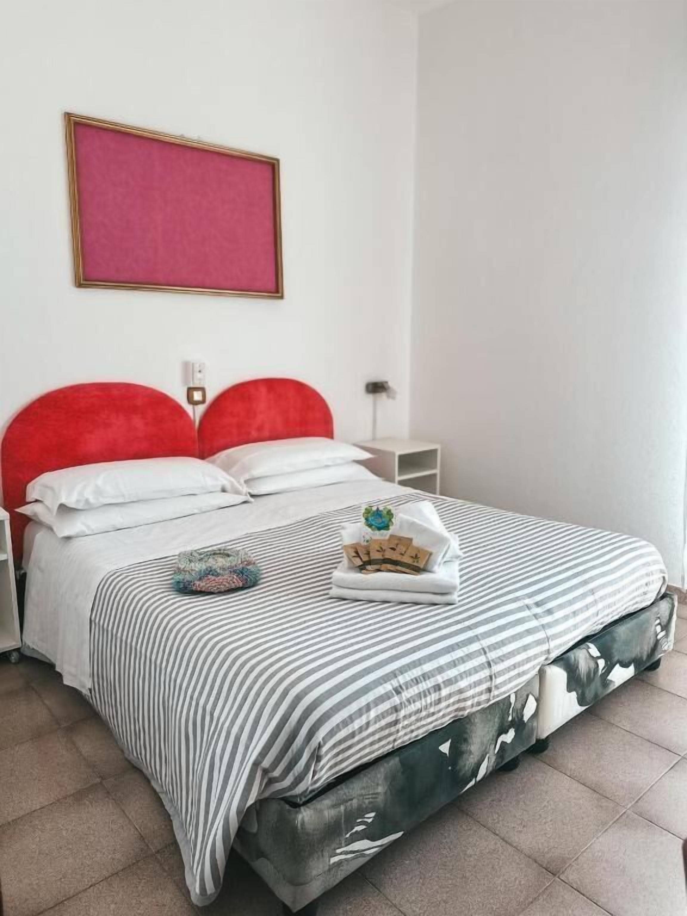 A neatly made bed with striped bedding, a red headboard, and a pillow with a floral design.