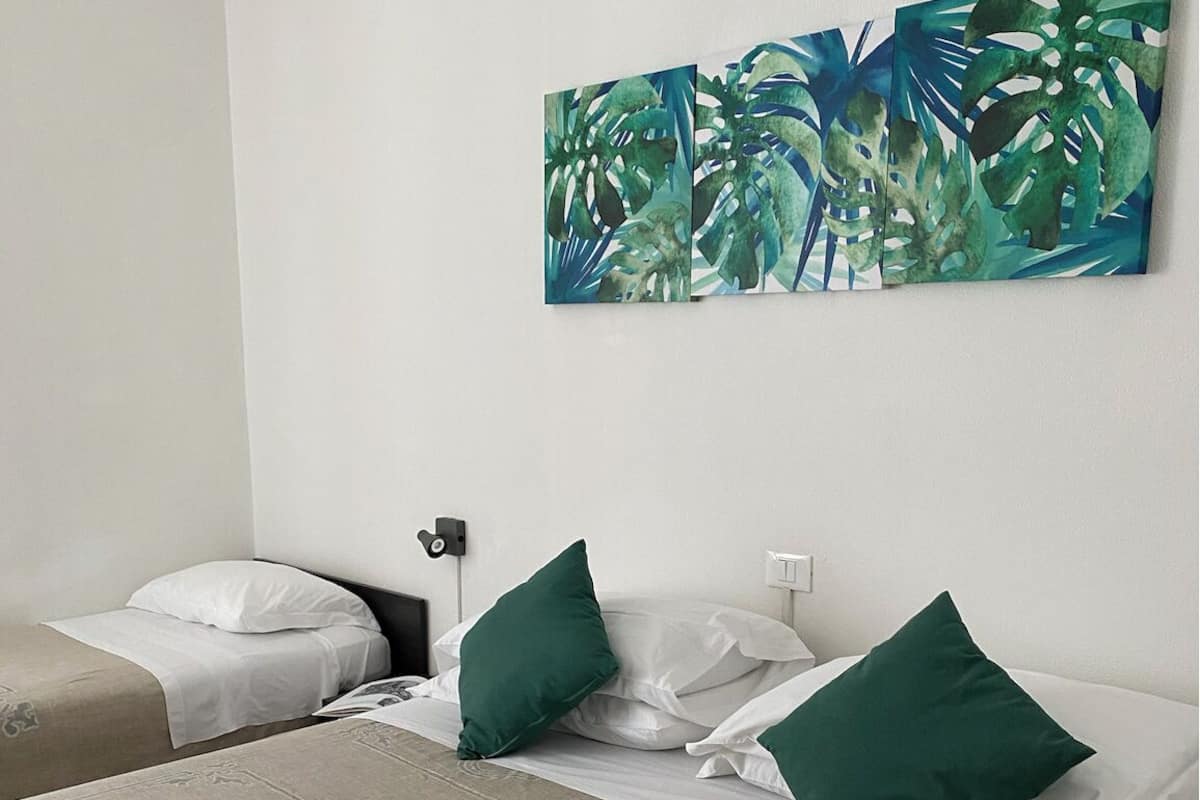 A hotel room with two beds, a large tropical artwork on the wall, and neatly folded towels on the bed.