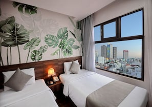 A hotel room with two beds, a city view, and a wall mural of tropical leaves.
