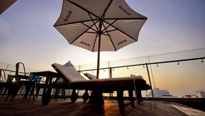 A rooftop terrace with a large umbrella, lounge chairs, and a view of the city skyline at sunset. - Mega Light Hotel (Bac Nha Trang)