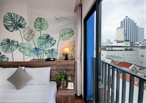 A hotel room with a bed, a nightstand, a lamp, and a view of a cityscape through a balcony. - Mega Light Hotel (Bac Nha Trang)