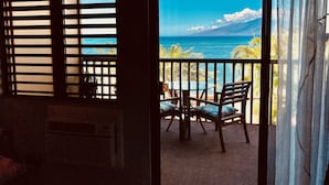 A room with a view of the ocean through a window with blinds.