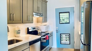 A modern kitchen with stainless steel appliances, grey cabinetry, and a wooden floor.