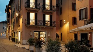A multi-story building with balconies, a cobblestone street, and outdoor seating. - Cavour 1 - New apartment at the lake (Salò)