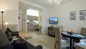 A modern living room with a sofa, dining table, and chairs, a kitchen in the background, and a TV on the wall. - Cavour 1 - New apartment at the lake (Salò)