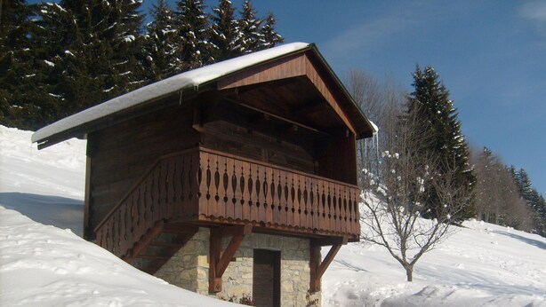 Una cabaña de madera con balcón, rodeada de nieve y árboles.