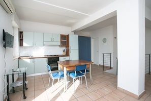 A compact kitchen with a dining table and chairs, a small table with a chair, and a clock on the wall.