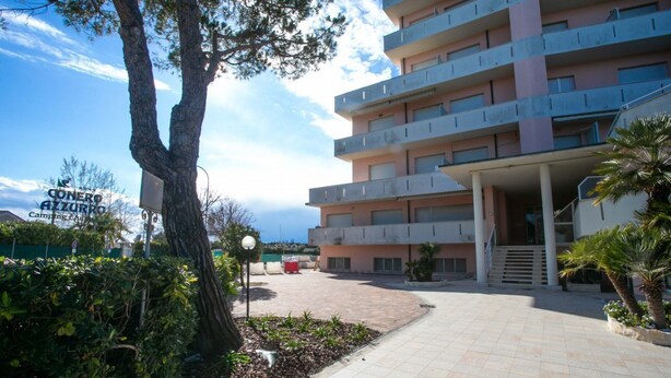 Un hôtel à plusieurs étages doté d’une cour intérieure, d’un espace extérieur aménagé et d’une enseigne indiquant « Conero Alzurra Camping ».