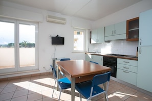 Una cocina con una mesa de comedor y sillas, un televisor montado en la pared y vistas a través de una puerta corrediza de vidrio.