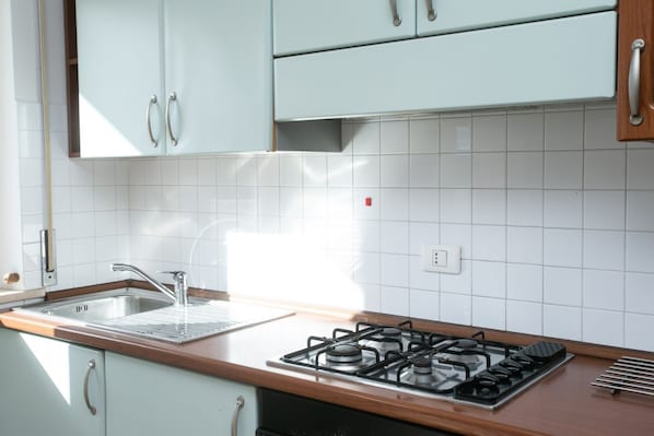 Una cocina con gabinetes blancos, un lavamanos de acero inoxidable y una estufa a gas.