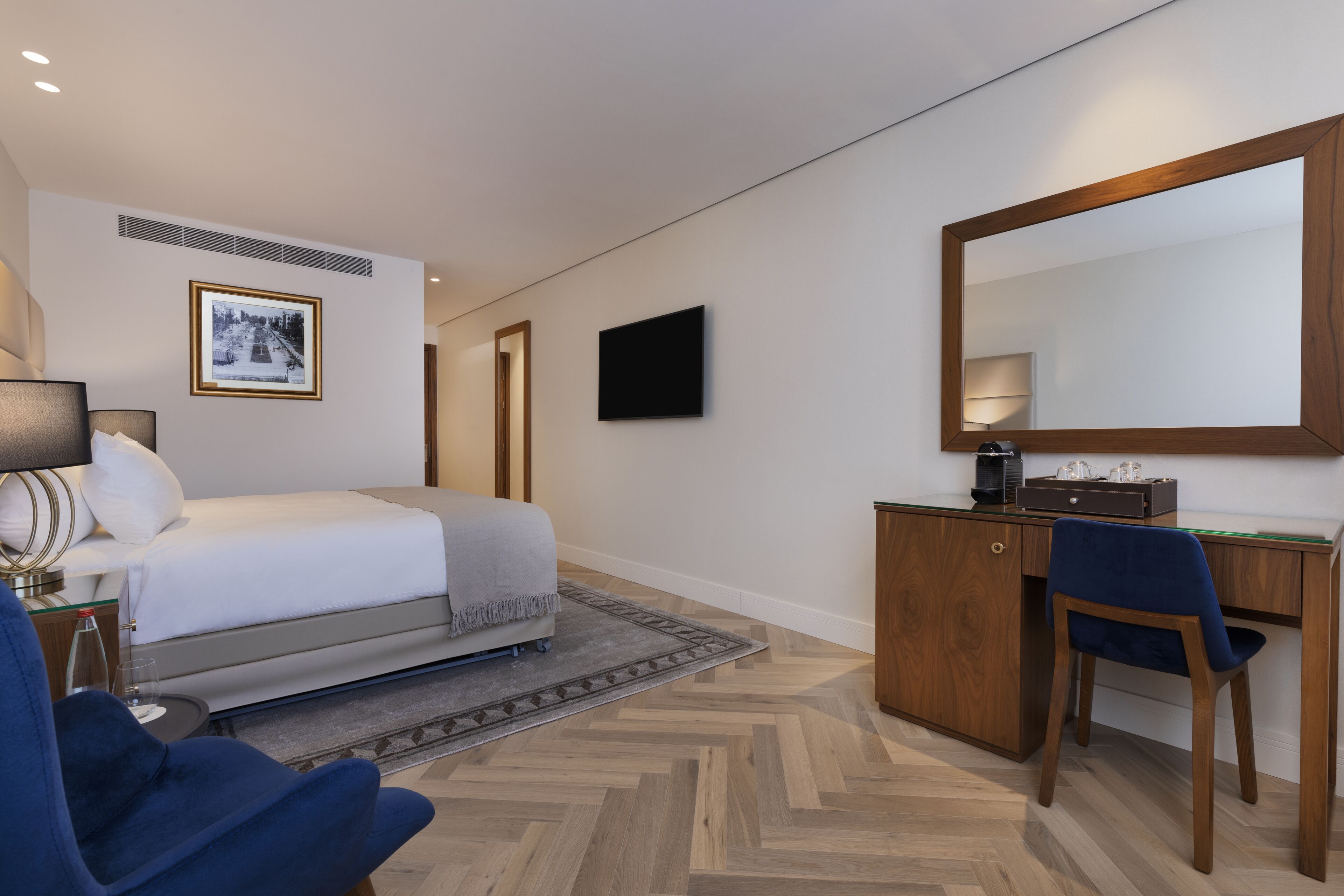 Une chambre d’hôtel avec un lit, un bureau, une chaise et un grand miroir.