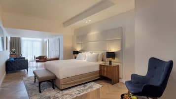 A modern hotel room with a large bed, a desk, a chair, and a dining table with fruit.