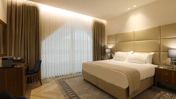 A hotel room with a large bed, a desk, a chair, and a bedside table with lamps.