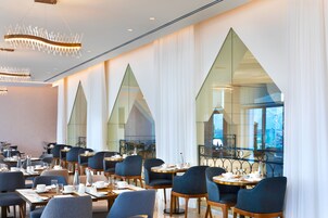 A modern dining area with tables and chairs, large windows, and a geometric ceiling design.
