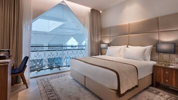 A modern hotel room with a large bed, a desk, and a view of a balcony with a railing.