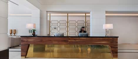 A modern reception desk with a wooden finish, a geometric patterned divider, and a glass lower section.