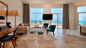 A modern hotel room with a large window offering a beach view, a sofa, a desk with a lamp, and two chairs. - Herbert Samuel Opera Tel Aviv (Tel Aviv)