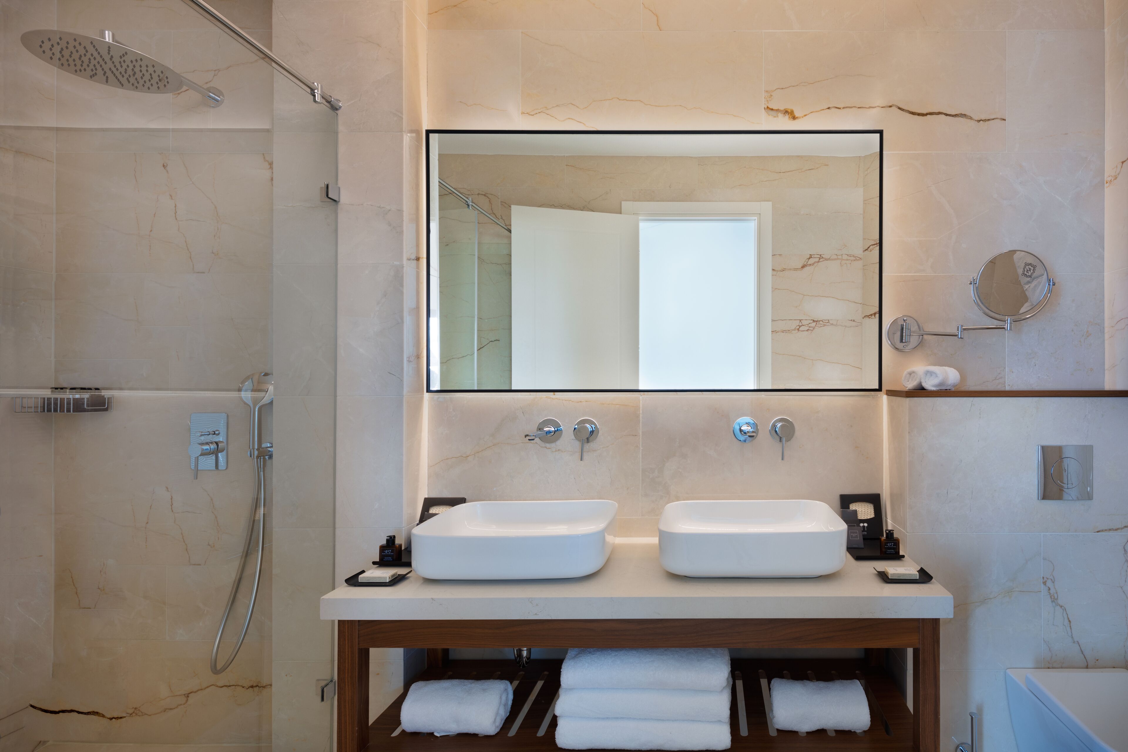 A modern bathroom with two sinks, a shower, and a mirror above the sinks.