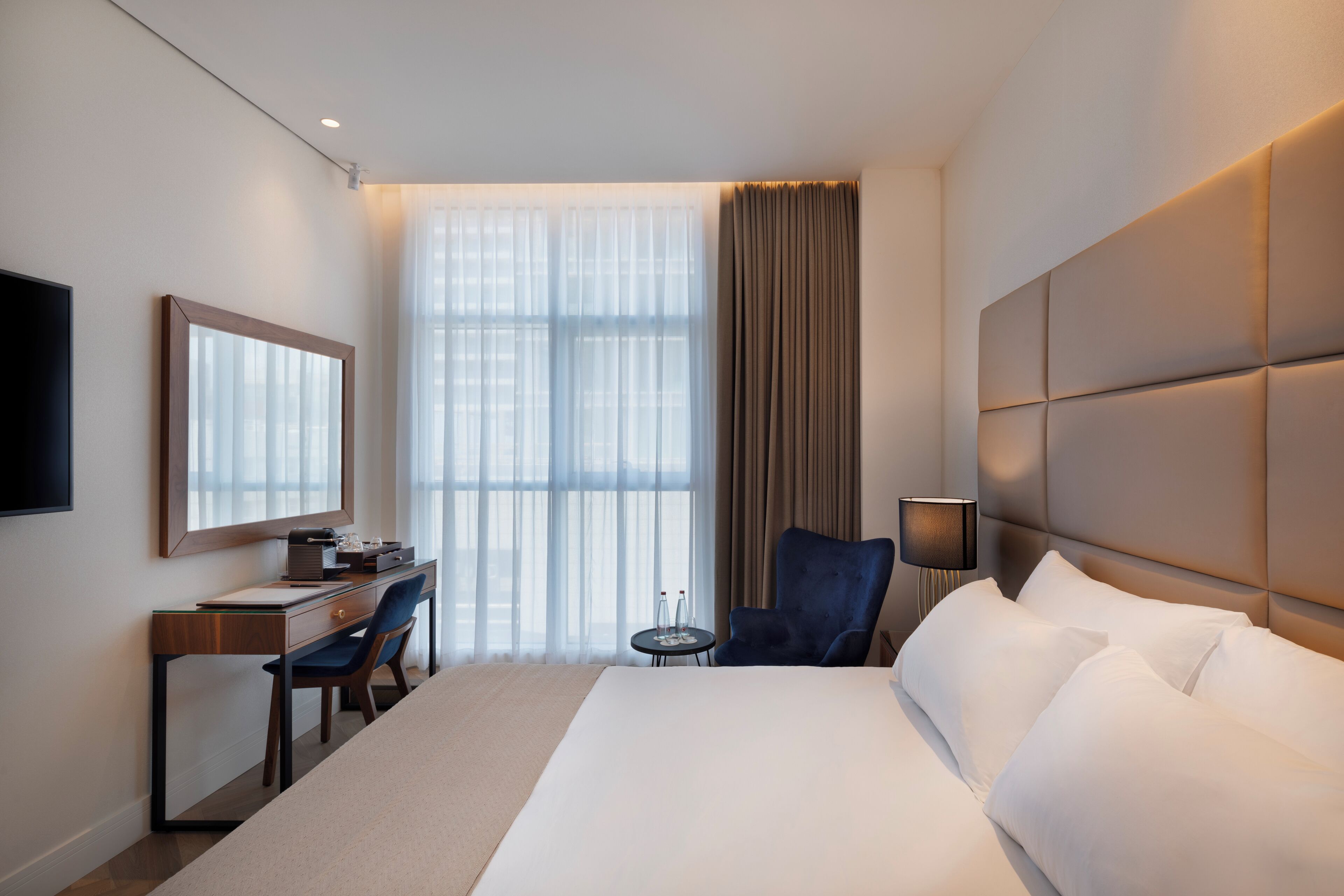 A hotel room with a large bed, a desk with a chair, a television, and a window with curtains.