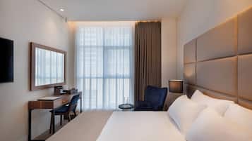 Habitación de hotel con una cama grande, un escritorio con silla, un televisor y una ventana con cortinas.